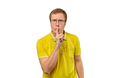 Téléchargez les photos : Funny young man in yellow T-shirt asking to be quiet, silence gesture isolated on white background. Young man in glasses saying Shhh, keep quiet, please and making silence gesture, request for silence - en image libre de droit