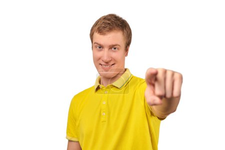 Téléchargez les photos : Smiling attractive guy in casual yellow T-shirt pointing finger forward isolated on white background. Funny young handsome man pointing forward, indicates goal, guy pointing at camera - en image libre de droit