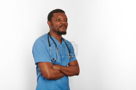 Téléchargez les photos : Black surgeon doctor bearded man in blue coat with crossed arms isolated on white background copy space. Serious adult black african american practicing surgeon portrait, confident look to right - en image libre de droit