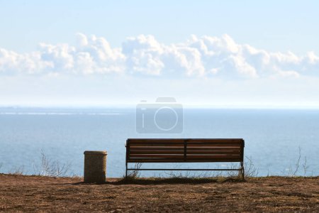 Foto de Empty bench with trashcan on cliff before sea background, peaceful and quiet place for thinking alone, loneliness and loss of loved one concept. Pacifying view of marine horizon of Azov sea copy space - Imagen libre de derechos