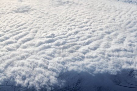 Téléchargez les photos : Over clouds top view from aircraft window, thick white blue clouds looks like soft foam, overcast with fresh frosty air. Beautiful cloudy sky view to troposphere, heavy cloudiness - en image libre de droit