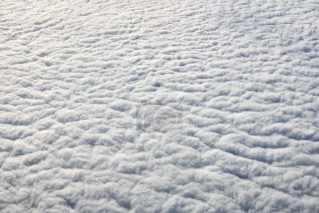 Téléchargez les photos : Breathtaking over clouds view from aircraft window, thick white blue clouds looks like soft foam, overcast with fresh frosty air. Beautiful cloudy sky view to troposphere, heavy cloudiness - en image libre de droit