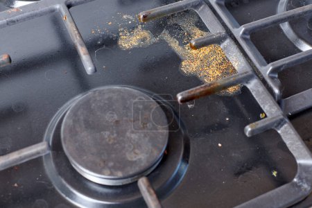Foto de Unclean dirty kitchen black stove after soup boil over, dried food spots, fat stains dry food leftovers. Black stainless cooktop with gas burner stained in remains of fat food and oil splatters - Imagen libre de derechos