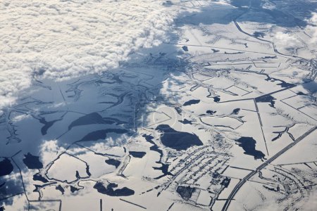 Aerial view over clouds top to snow covered rivers, fields and roads, winter fresh frosty air. Beautiful hazed sky aerial view to Earth troposphere, snowy abstract background texture