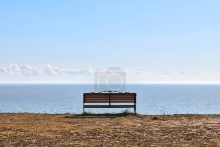 Foto de Empty bench on cliff before sea background, peaceful and quiet place for thinking alone, loneliness and loss of loved one concept. Pacifying view of marine horizon of Azov sea in Russia - Imagen libre de derechos