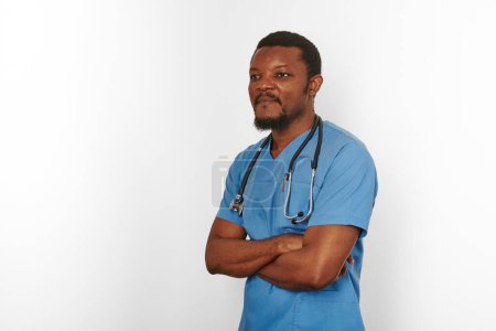 Téléchargez les photos : Black surgeon doctor bearded man in blue coat with crossed arms isolated on white background copy space. Serious adult black african american practicing surgeon portrait, confident look to left - en image libre de droit