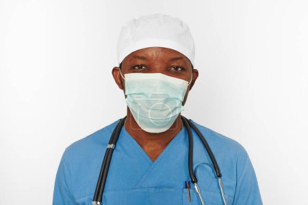 Téléchargez les photos : Black surgeon doctor man in blue coat white cap and surgeon mask with stethoscope isolated on white background. Focused adult black african american practicing surgeon portrait, concentrated look - en image libre de droit