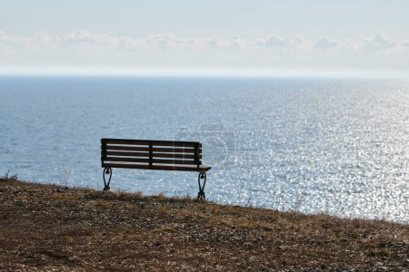 Foto de Empty bench on cliff before sea background, peaceful and quiet place for thinking alone, loneliness and loss of loved one concept. Pacifying view of marine horizon of Azov sea in Russia, copy space - Imagen libre de derechos