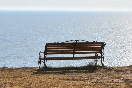 Foto de Empty bench on cliff before sea background, peaceful and quiet place for thinking alone, loneliness and loss of loved one concept. Pacifying view of marine horizon of Azov sea in Russia - Imagen libre de derechos