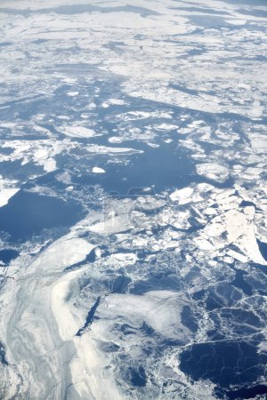 Téléchargez les photos : Aerial view from airplane window over clouds top to snow covered frozen sea, winter fresh frosty air. Beautiful hazed sky aerial view to Earth, snowy background texture - en image libre de droit