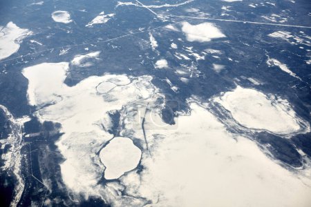 Téléchargez les photos : Aerial view from airplane window over clouds top to snow covered rivers, fields and roads, winter fresh frosty air. Beautiful hazed sky aerial view to Earth troposphere, snowy background texture - en image libre de droit