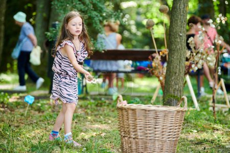 Photo for Svetlogorsk, Russia - 13.08.2022 - Young little girl throws spruce cones into basket, funny children game in public park, green forest background. Cute attractive young lady plays in park - Royalty Free Image
