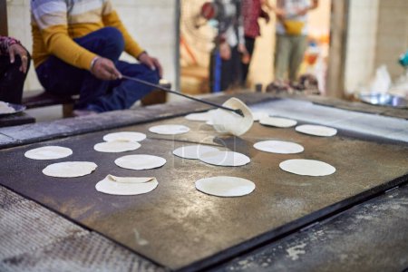 Photo for Cooking of chapati round flatbreads for langar in sikh gurudwara temple, many uncooked roti flatbreads made from stoneground whole wheat flour, traditional indian cheap unleavened bread - Royalty Free Image