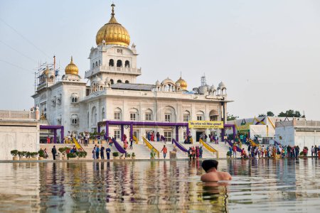 Photo for New Delhi, India - 10.11.2022 - Sikh prays in holy pond Sarovar of Gurudwara Bangla Sahib temple in New Delhi, back view of Sikh pilgrim stays in water worships in popular touristic spot in Delhi - Royalty Free Image
