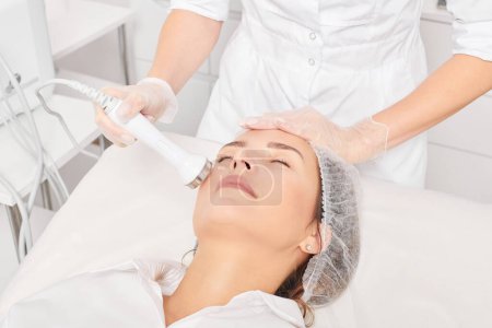 Kosmetikerin macht Ultraschall Hautstraffung für Verjüngung Frauengesicht mit Phonophorese, Anti-Aging-kosmetische Verfahren mit in Beauty-Spa-Salon. Kosmetikerin macht Ultraschall-Hautpflege