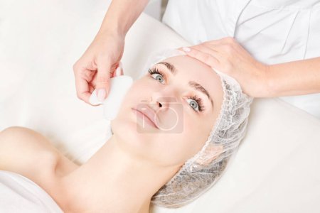 Photo for Beautician making facial massage with Gua Sha stone of woman face skin for lymphatic drainage, anti aging skincare cosmetic procedure in beauty spa salon. Face massage with Gua Sha tool - Royalty Free Image