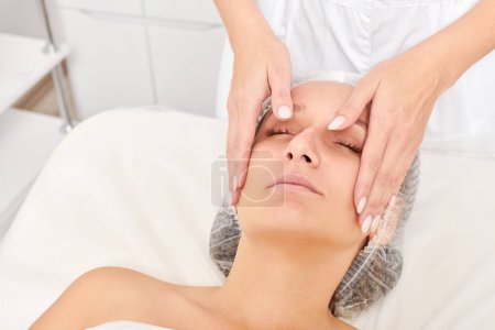 Beautician massages woman face skin for rejuvenation, anti aging skincare cosmetic procedure in beauty spa salon. Cosmetologist making facial massage with cosmetic cream for beautiful female face
