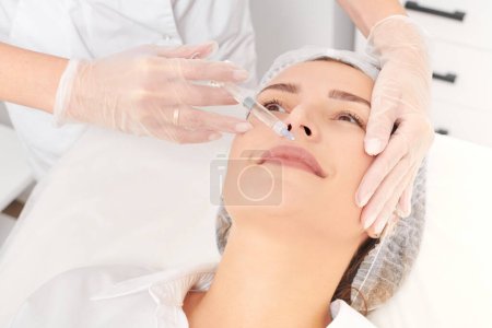 Photo for Cosmetologist makes fillers injection for lips augmentation and volume, non surgical cosmetic procedure in beauty salon. Beautician specialist hands in gloves makes lips injection with syringe - Royalty Free Image