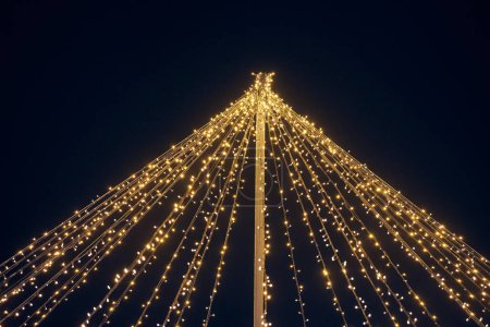 Gelbe Lichtergirlanden im Freien hängen Drähte von Säule bei nachtblauem Himmel Hintergrund, magische Urlaubsatmosphäre. Festliche Weihnachtsgirlanden mit leuchtend gelbem Licht, schöne Außendekoration