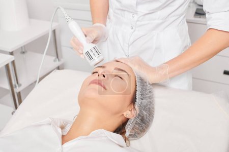 Kosmetikerin macht Kryotherapie für Verjüngung Frauengesicht, Anti-Aging-kosmetische Verfahren mit in Beauty-Spa-Salon. Kosmetologe macht Kryo-Therapie Lifting mit zur Hautverjüngung und Glättung