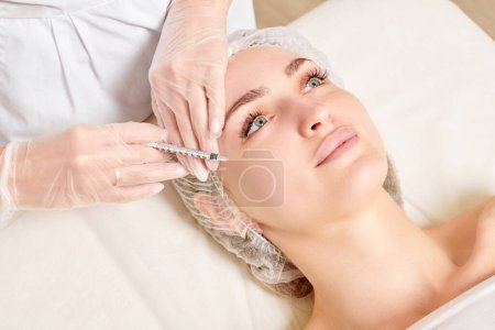 Cosmetologist makes rejuvenation injection in woman face, anti aging non surgical cosmetic procedure in beauty salon. Beautician specialist hands in gloves makes treatment injection with syringe