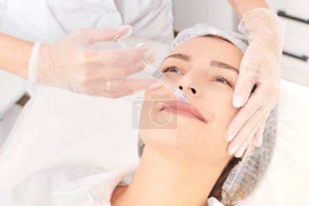 Photo for Cosmetologist makes fillers injection for lips augmentation and volume, non surgical cosmetic procedure in beauty salon. Beautician specialist hands in gloves makes lips injection with syringe - Royalty Free Image