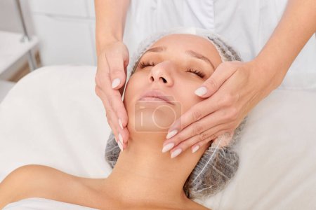 Kosmetikerin massiert Frau Gesichtshaut zur Verjüngung, Anti-Aging-Hautpflege kosmetische Verfahren im Beauty-Spa-Salon. Kosmetikerin macht Gesichtsmassage mit kosmetischer Creme für schönes weibliches Gesicht