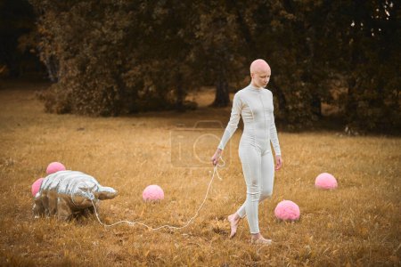Photo for Portrait of young hairless girl with alopecia in white cloth walking tardigrade toy in fall park, surreal scene with bald teenage girl reflect on intertwining threads of life and art - Royalty Free Image