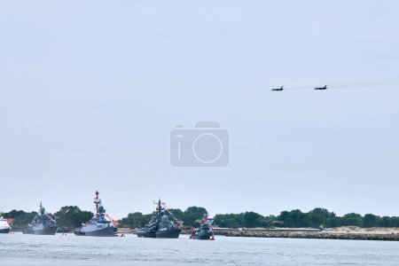 Photo for Military fighter jets are flying over Russian naval forces parade warships along coastline, seafaring tradition of military ships formation at Navy Day, nautical spectacle of russian sea power - Royalty Free Image