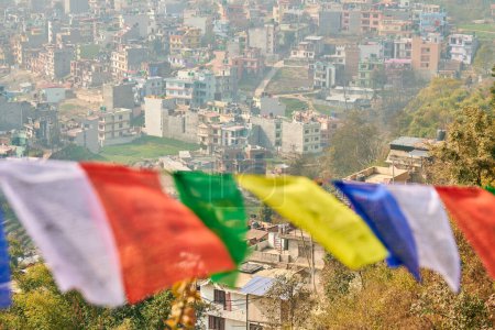 Blick auf Kathmandu mit vielen Flachbauten durch bunte Gebetsfahnen, Blick auf das Stadtbild von Kathmandu auf den Hügeln, die eine harmonische Mischung aus Spiritualität und Urbanität schaffen