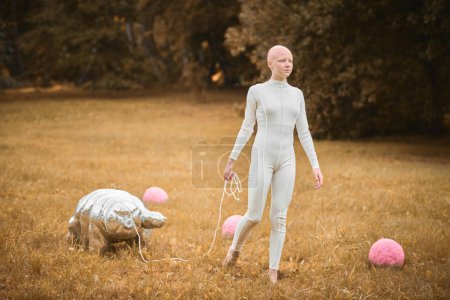 Téléchargez les photos : Portrait de jeune fille sans cheveux avec alopécie en tissu blanc marchant jouet tardif dans le parc d'automne, scène surréaliste avec une adolescente chauve réfléchir sur les fils entrelacés de la vie et de l'art - en image libre de droit