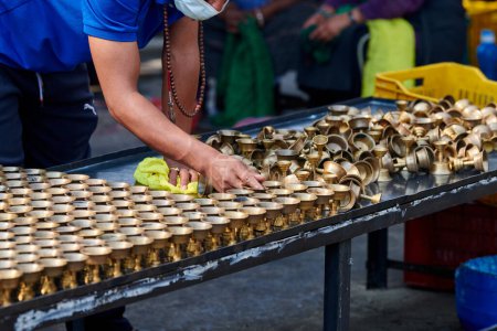Nepalesisches Tempelpersonal gießt Kerzenöl aus, nachdem Docht ausbrennt, um ersetzt zu werden, Reinigung von Bronze-Kerzenhaltern wird wiederverwendet, ehrenamtlicher Einsatz für den Boudhanath Stupa Tempel in Kathmandu
