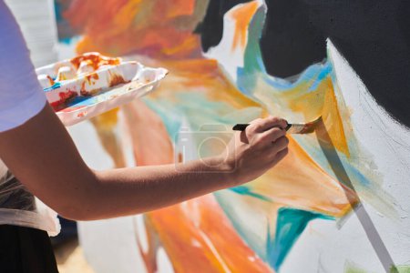 Female painter hand passionately paints picture with paintbrush for outdoor street exhibition using vibrant colors, close up view
