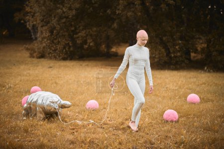 Portrait de jeune fille sans cheveux avec alopécie en tissu blanc marchant jouet tardif dans le parc d'automne, scène surréaliste avec une adolescente chauve réfléchir sur les fils entrelacés de la vie et de l'art