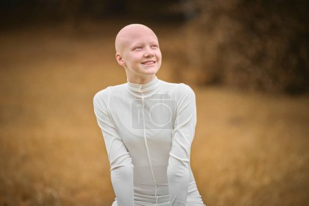 Portrait of young happy hairless girl with alopecia in white cloth on autumn park background, radiant smile of bald pretty teenage girl symbolizing joy acceptance individuality and her unique beauty