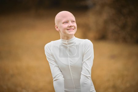 Retrato de la joven chica feliz sin pelo con alopecia en tela blanca en el fondo del parque de otoño, sonrisa radiante de la chica adolescente bonita calva que simboliza la individualidad aceptación de la alegría y su belleza única