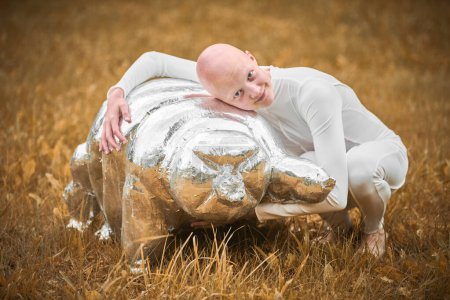 Portrait of young hairless girl with alopecia in white cloth hugging figure of tardigrade in autumn park background, bald pretty teenage girl highlighting beauty found in embracing vulnerability