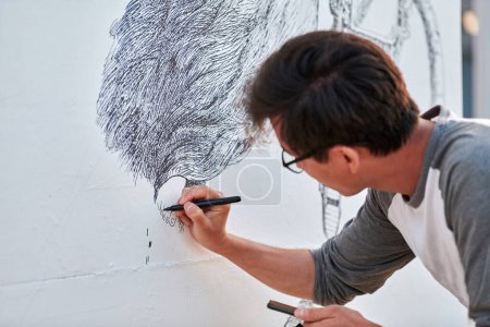 Young male painter passionately paints picture with black permanent marker for outdoor street exhibition using only black color, visual spectacle through expressive brush strokes