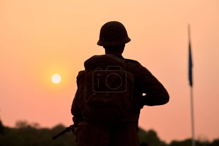 Rear view of silhouette of soldier statue in military gear holds weapon against glorious sunset, symbolizing powerful and patriotic scene of dedication and sacrifice