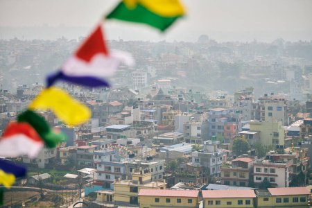 Vue de Katmandou avec beaucoup de bâtiments de faible hauteur à travers des drapeaux de prière colorés, vue sur la colline du paysage urbain de Katmandou créant un mélange harmonieux de spiritualité et d'urbanité