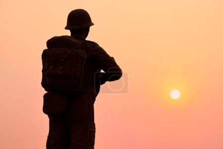 Rear view of silhouette of soldier statue in military gear holds weapon against glorious sunset, symbolizing powerful and patriotic scene of dedication and sacrifice