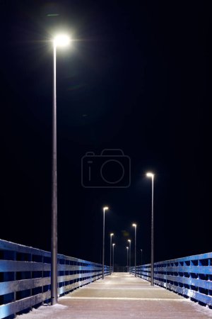 Lampposts along pier going into night darkness above sea symbolize serene scene of calmness cold winter night, minimalist geometry of pier in calming night sky, pier to open sea without people
