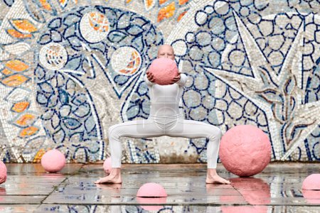 Junges haarloses Mädchen mit Alopezie im weißen futuristischen Anzug tanzt im Freien und hält sanft rosa Ball auf abstraktem Mosaik sowjetischen Hintergrund, symbolisiert Selbstausdruck und kulturelle Identität