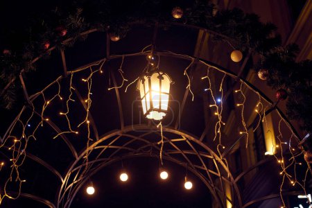 Weihnachtsbeleuchtung, die den Torbogen in der Silvesternacht schmückt, verleiht der nächtlichen Szenerie ein gemütliches Ambiente, gelbes geheimnisvolles Licht, das festliches Staunen und Freude hervorruft, magische Neujahrsatmosphäre