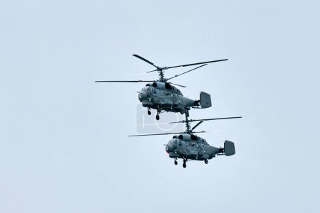 Two Russian military helicopters armed with missiles flies in blue sky, airborne mission of gunships with targeting system performs an aerial maneuvers for military operation, russian aviation