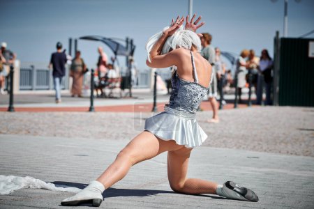 Junge sexy Mädchen im silbernen Mikrorock tanzen mit sanften, femininen und anmutigen Bewegungen, weibliche Outdoor-Tanzdarbietungen auf der Strandpromenade schaffen ein aufregendes Outdoor-Spektakel