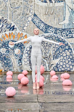 Jeune fille sans cheveux ballerine avec alopécie en costume futuriste blanc dansant en plein air et saute parmi les sphères roses sur fond abstrait mosaïque soviétique, symbolise l'expression de soi