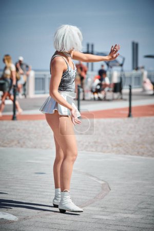Foto de Joven chica sexy en el espacio micro falda de plata bailando con movimientos suaves, femeninos y elegantes, actuación de danza al aire libre femenina en el paseo marítimo creando un espectáculo al aire libre excitante - Imagen libre de derechos