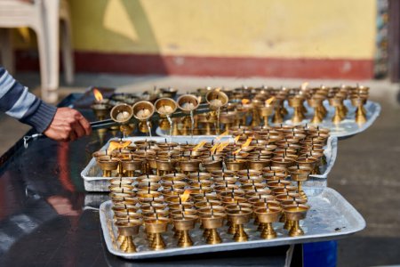 El personal del templo nepalí vierte aceite de vela después de que la mecha se queme para su reemplazo, limpiando la reutilización de los candelabros de bronce, el trabajo voluntario en el templo Boudhanath Stupa en Katmandú