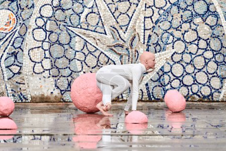 Joven bailarina sin pelo con alopecia en traje futurista blanco bailando al aire libre entre esferas rosadas sobre fondo abstracto mosaico soviético, simboliza la expresión de sí mismo y la aceptación de la belleza única